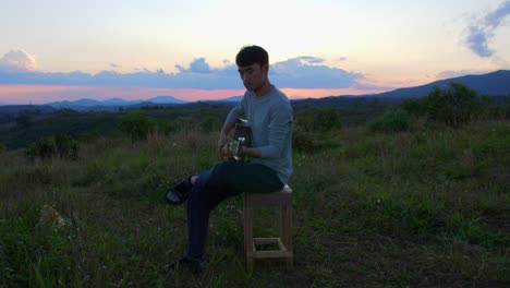 Male-musician-playing-guitar-at-dusk-with-mountains-and-horizon-in-background,-Vietnam