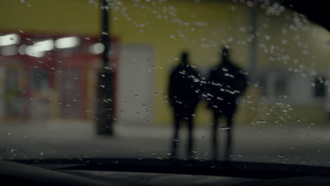 Silhouette-of-Guys-Walking-at-Night-filmed-through-Windscreen-of-Car-with-Rain-Drops