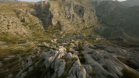 FPV-drone-shot-flying-downhill-over-winding-Sa-Calobra-road-along-rocky-mountain-range-in-Mallorca,-Spain-during-evening-time