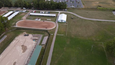 Aerial-sliding-shot-of-Wayne-County-Fairgrounds,-horses-riding-in-an-outdoor-arena