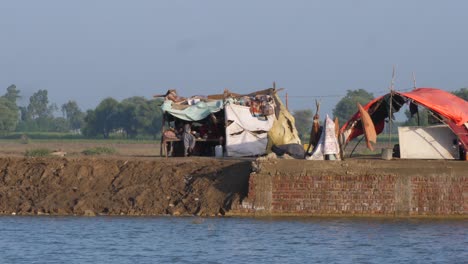 Shot-of-makeshift-camps-in-the-background-with-flood-water-flowing-in-the-front-in-Sindh,-Pakistan-on-a-sunny-day