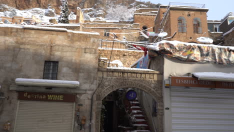 In-the-old-center-of-Mardin,-we-see-the-shops-lined-up-in-the-Artuklu-bazaar-in-front-and-behind-them,-we-see-historical-stone-mansions