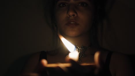 A-woman-in-the-dark-house-with-a-lit-candle-in-her-hands-moving-the-candle-looking-into-the-camera