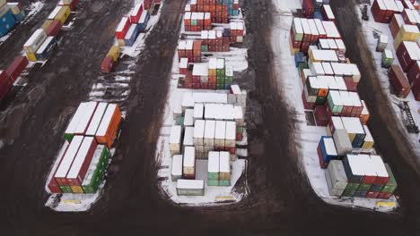 Forwarding-shot-of-snow-covered-shipping-containers-on-a-winter-day,-stacked-on-each-other,-Aerial-view