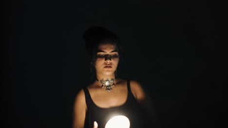 Front-view-of-woman-in-black-dress-moving-towards-into-the-camera-in-the-dark-and-suddenly-drops-a-burning-candle-in-her-hands