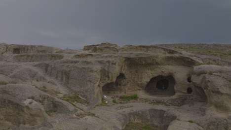Drone-shot-of-an-ancient-naturally-formed-series-of-caves-in-barren-deserted-Georgia-Region,-featuring-ruins-of-abandoned-historical-civilisation