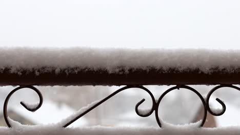 Metal-forged-fence-with-decorative-shapes-covered-in-snow-during-snowfall