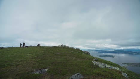 Excursionistas-Con-Perro-Doméstico-En-La-Cima-De-La-Montaña-De-Lurøyfjellet-Con-Cielo-Nublado-En-Noruega
