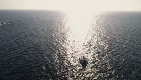 Aerial-View-of-Catamaran-Sailing-in-Aegean-Sea-by-Santorini-Island,-Greece-on-Golden-Hour-Sunlight