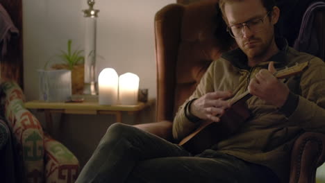 A-man-on-an-armchair-at-night-is-relaxing-and-playing-a-ukulele