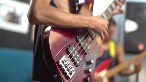Close-up-of-hand-playing-red-electric-bass,-guitarist-in-background