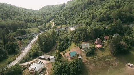 Dynamic-aerial-view-with-FPV-racing-drone-flying-above-cottages-and-under-an-old-railway-bridge-alongside-an-empty-winding-road