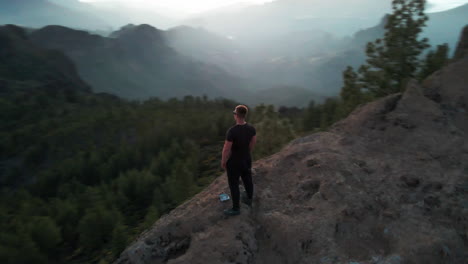 Empowering-aerial-shot-of-confident-guy-standing-on-the-edge-of-a-cliff-in-Gran-Canaria-during-the-sunset