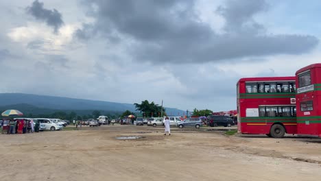 Experience-the-hustle-and-bustle-of-a-hillside-bus-terminal-in-Bholaganj,-Sylhet,-Bangladesh,-as-travelers-embark-on-their-journeys-amidst-a-backdrop-of-lush-green-hills