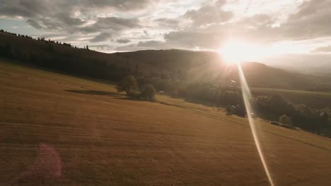 Aerial-footage-from-an-action-camera-flying-low-into-the-sunset-approaching-lone-trees-and-turning-up-the-hill-covered-in-yellow-dry-grass