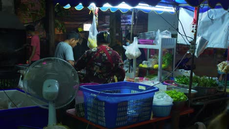 Street-vendor-selling-food-to-customers-at-night-with-traffic-during-rain-storm,-Thailand