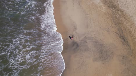 A-woman-walks-along-a-beach-as-seen-from-an-overhead-aerial-drone