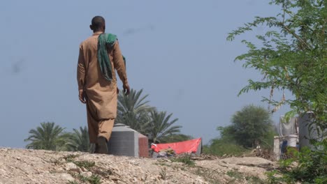 Low-angle-shot-of-a-local-walking-past-makeshift-roadside-camp-made-after-flooding-in-Sindh,-Pakistan-at-daytime