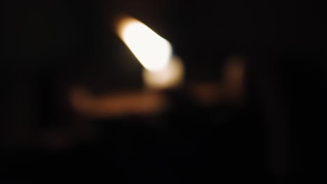 Die-Frau-Hält-Eine-Brennende-Kerzenflamme-Vor-Verschwommenem-Bokeh-Licht-Vor-Dunklem-Hintergrund,-Nahaufnahme