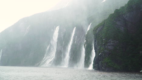 Dramatic-scenery-with-multiple-waterfalls-cascading-into-Milford-Sound,-rainy