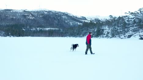 A-Man-With-His-Dog-Strolling-In-Winter-Snow-Landscape-In-Hildremsvatnet,-Norway
