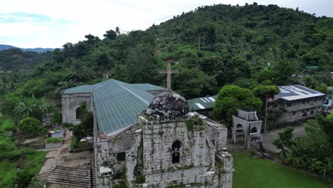 Aerial-Orbit-of-Idyllic,-Classic-Bato-Church-with-lush-jungles-and-nearby-rural-community