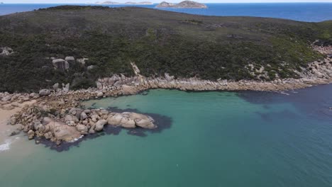 Drone-aerial-pan-up-over-beautiful-dark-blue-water-and-green-mountain-on-a-sunny-day-in-Wilsons-Promontory