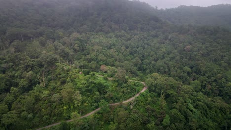 Epic-drone-shot-of-Jungle-Road-Surrounded-By-Mountain-Landscape-With-Dense-Forest-Jungle-In-Central-Sumbawa-Island,-Indonesia