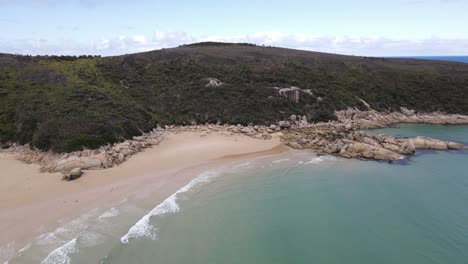 Drone-aerial-moving-forward-and-pan-up-over-beautiful-light-blue-water-and-green-mountain-on-a-sunny-day-in-Wilsons-Promontory