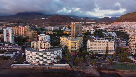 Establisher-aerial-of-hotels-facing-vast-beach-in-Los-Cristianos,-Tenerife