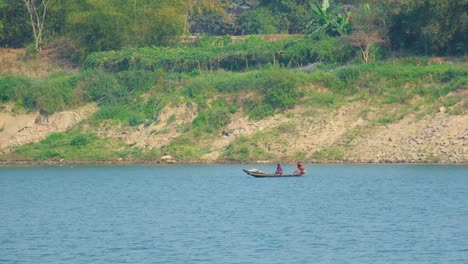 Two-Asian-fishermen-paddle-a-traditional-boat-on-a-big-river,-enjoying-the-scenic-beauty-and-tranquility-of-nature
