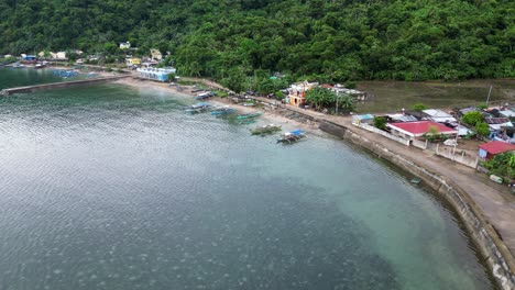 Stunning-Aerial-View-of-Idyllic,-seaside-Rural-Village-with-lush-jungles,-transparent-ocean-waters-and-fishing-boats