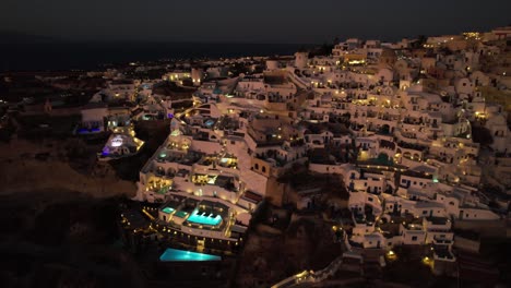 Aerial-View-of-Santorini-Island-at-NIght,-White-Buildings-and-Swimming-Pools-in-Lights
