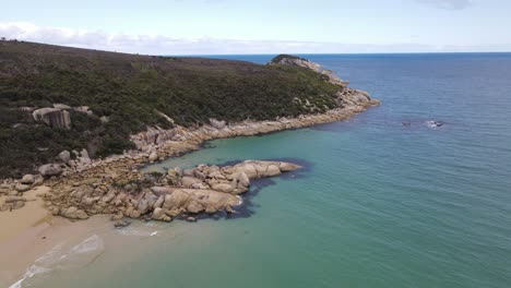Drone-aerial-moving-forward-and-pan-up-over-beautiful-light-blue-beach-and-green-mountain-on-a-sunny-day-in-Wilsons-Promontory