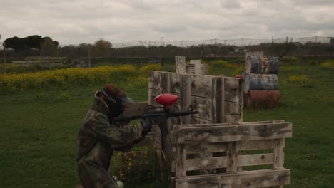 A-woman-sheltered-behind-some-wooden-pallets-in-a-paintball-field-under-a-cloudy-sky