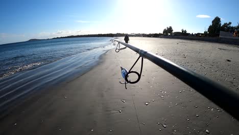 POV-of-fishermen-holding-pole-crankbait-lure-attached-to-guide,-walking-on-beach