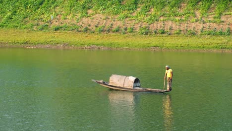 An-Asian-fisherman-navigates-his-small-boat-on-the-Surma-river-at-sunset,-capturing-the-serene-beauty-of-the-soft-light-on-the-water