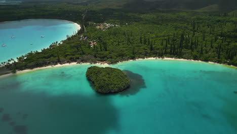 Kanumera-Bay,-Isle-of-Pines'-crystal-clear-water,-pristine-beach,-and-the-Sacred-Rock-islet---aerial-pull-back-reveal