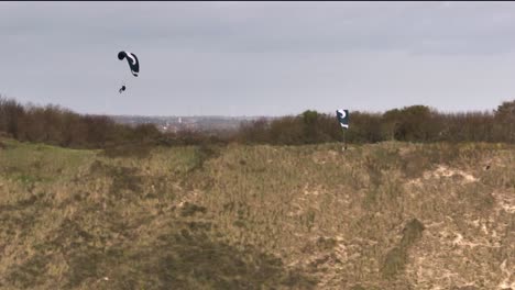 Two-experienced-paragliders-soar-along-coastal-dunes,-adrenaline-sport