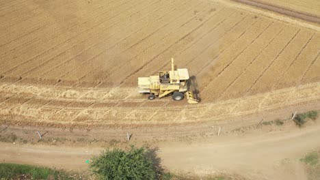 Aerial-drone-shot-over-a-yellow-agricultural-farm-combine-harvester-busy-harvesting-wheat-on-an-industrial-wheat-field-on-a-sunny-day