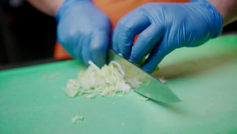 Hands-with-plastic-gloves-chop-lettuce-with-knife-in-kitchen,-close-up