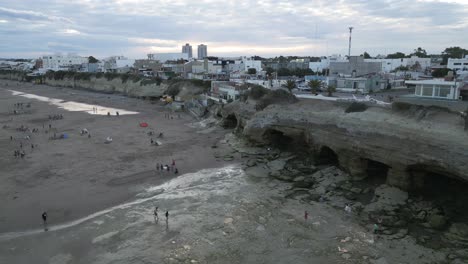 Aerial-Drone-Fly-Above-Argentine-Patagonian-Cliff-Beach-Caves,-Las-Grutas-Sea-Coast-City-in-Rio-Negro,-People-Walk-on-White-Sand
