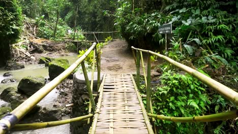 Bamboo-bridge-crosses-tropical-river-and-waterfall-in-view-from-hiking-path