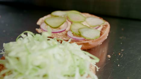 Pickles-and-lettuce-on-burgers-being-put-together-in-kitchen,-close-up