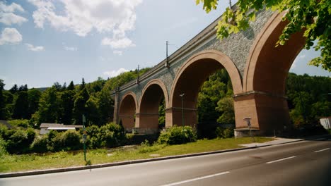 Viadukt-Schwarza-Mit-Vorbeifahrenden-Motorrädern-Und-Autos-Im-Vordergrund-Und-Bäumen,-Die-Die-Rechte-Seite-Des-Viadukts-Verdecken