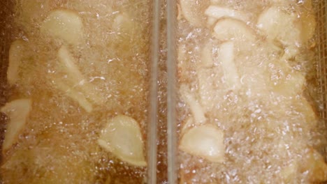 Closeup-of-potato-pieces-deep-fried-in-baskets-in-oil,-vertical-motion