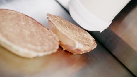 Appliance-puts-white-sauce-on-burger-buns-in-kitchen,-handheld-closeup