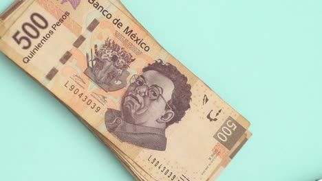 Primer-Plano-De-La-Mano-Colocando-Una-Pila-De-Billetes-Mexicanos-De-500-Pesos-En-La-Mesa-Azul