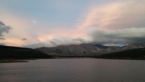 Aerial-Drone-Fly-Close-to-Dreamy-Lagoon-Patagonian-Landscape,-Pink-Blue-Sky-and-Reflective-Water-between-Hills,-Moon-Shines-High,-La-Zeta-Lake,-Argentina