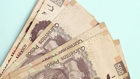 Vertical-close-up-of-Mexican-500-Peso-bills-placed-on-blue-surface